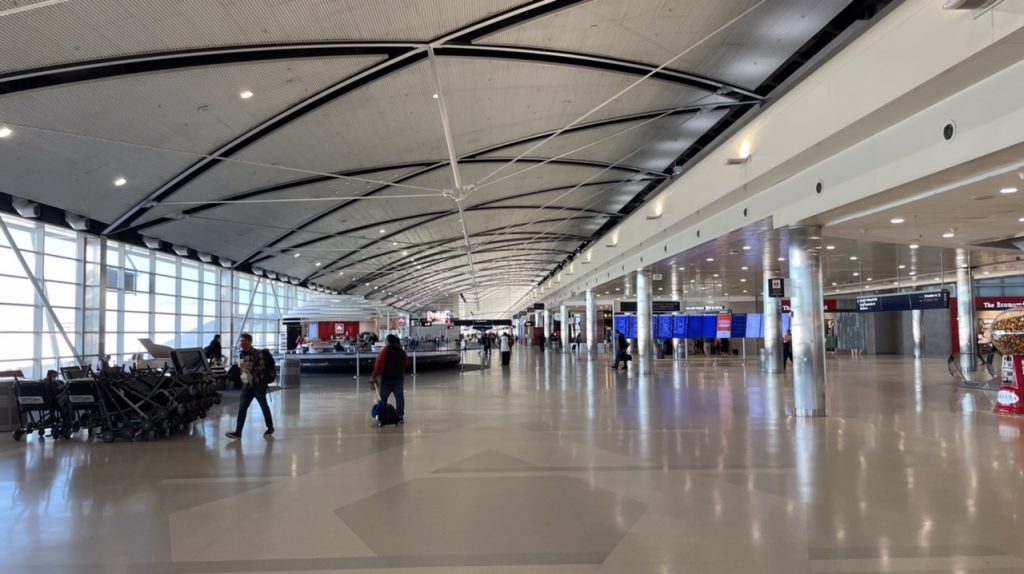 The center of Concourse A at DTW’s McNamara Terminal. It is relatively early in the day and few people are walking around. The ceiling arches gracefully over the aisle.